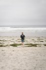 Мальчик, несущий кузов и уходящий в океан — стоковое фото