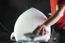 Hombre trabajando en una tabla de surf en un taller . - foto de stock