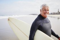 Hombre mayor llevando una tabla de surf . - foto de stock
