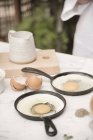 Dos sartenes con huevos frescos agrietados - foto de stock