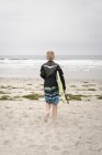 Niño llevando bodyboard y caminando en océano - foto de stock