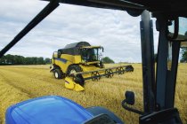 Combine harvester working alongside tractor — Stock Photo