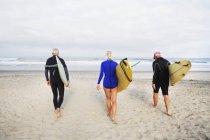 Senior woman and men carrying surfboards. — Stock Photo