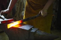 Blacksmith holds a length of hot metal — Stock Photo