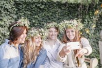 Mulheres com coroas de flores a tirar uma selfie . — Fotografia de Stock