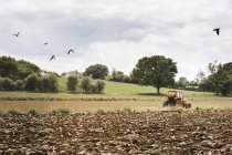 Ploughed field, and a tractor on the move. — Stock Photo