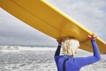 Senior woman carrying a surfboard — Stock Photo