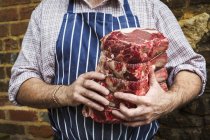 Açougueiro em avental segurando pedaço de carne — Fotografia de Stock