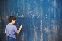 Boy writing in chalk on a chalkboard. — Stock Photo