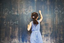 Girl writing in chalk on a chalkboard. — Stock Photo