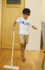 Niño con una fregona limpiando un piso de madera . - foto de stock