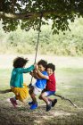 Meninos e menina sentado no balanço da árvore — Fotografia de Stock