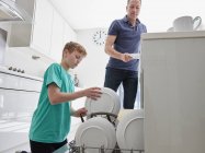 Мужчина и мальчик кладут тарелки в посудомоечную машину — стоковое фото