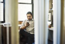 Чоловік сидить в офісі і перевіряє телефон — стокове фото