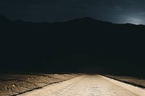 Chemin de terre dans le désert éclairé par des phares de voiture — Photo de stock