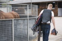 Homem transportando equipamento de equitação no estábulo de equitação — Fotografia de Stock