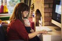 Mujer sentada con el bebé en el regazo usando la computadora - foto de stock