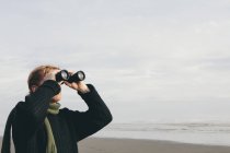 Mann steht am Strand und schaut durch Fernglas — Stockfoto