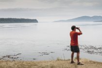 Mann steht am Strand und schaut durch Fernglas — Stockfoto