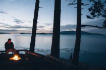 Homme assis près du feu de camp au crépuscule — Photo de stock