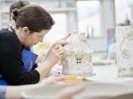 Woman working on decorated pottery cottage — Stock Photo