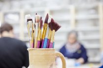 Pottery jug with paintbrushes. — Stock Photo