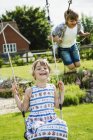 Boy and girl  on swings in garden. — Stock Photo