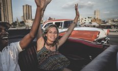Man and woman riding in classic convertible car with arms raised. — Stock Photo