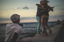 Pessoas dançando à beira-mar assistidas pelo homem — Fotografia de Stock