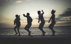 Чотири людини танцюють в черзі на фоні морської стіни — стокове фото