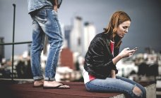 Женщина сидит и с помощью мобильного телефона — стоковое фото