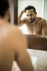 Hombre de pie frente al espejo del baño - foto de stock