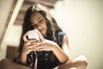 Девушка, сидящая, глядя на мобильный телефон — стоковое фото