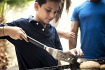 Boy turning food on barbecue. — Stock Photo