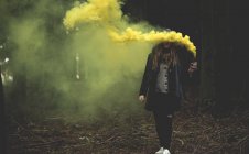 Mujer sosteniendo bengalas de humo amarillo en el bosque . - foto de stock