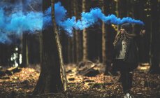 Woman holding blue smoke flare in forest. — Stock Photo