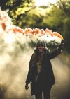 Femme tenant une fusée de fumée orange dans la forêt . — Photo de stock
