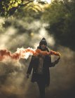 Femme tenant une fusée de fumée orange dans la forêt . — Photo de stock