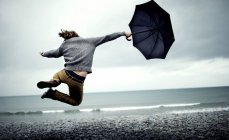 Человек держит зонтик, прыгает по пляжу — стоковое фото