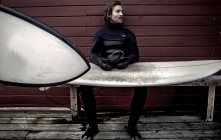 Surfista che indossa muta seduta vicino alla costruzione — Foto stock
