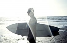 Man in wetsuit carrying surfboard. — Stock Photo