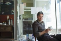 Зрілий чоловік сидить у кав'ярні з чашкою — стокове фото