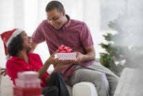 Man giving woman Christmas present while sitting on sofa in room interior — Stock Photo