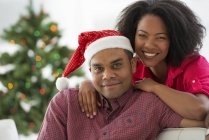 Couple afro-américain posant avec le chapeau de Père Noël devant l'arbre de Noël — Photo de stock