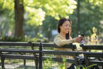 Mujer asiática revisando smartphone en banco del parque - foto de stock