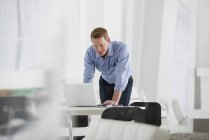 Hombre de pie en el escritorio y utilizando un ordenador portátil en la oficina - foto de stock