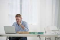 Mann sitzt am Schreibtisch und benutzt Laptop im Büro — Stockfoto