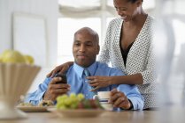 Чоловік перевіряє смартфон за сніданком з жінкою за випрямленням краватки — стокове фото