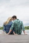 Man and woman sitting close together on lake pier — Stock Photo