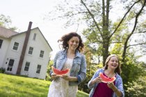 Woman with daughter walking on lawn with watermelon slices — Stock Photo